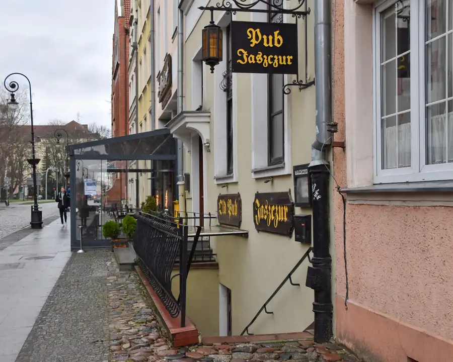 Ulica Wigilijna w Elblągu z czarnym szyldem Pub Jaszczur i latarnią na wysięgniku