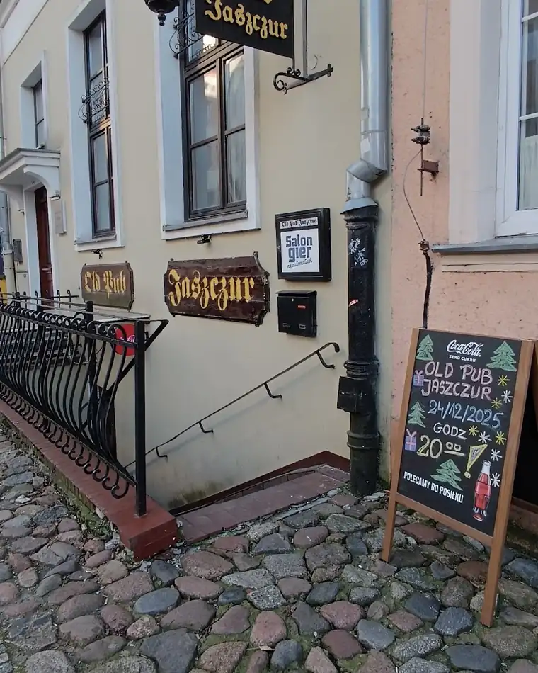 Wejście do Old Pub Jaszczur: kuta balustrada, schody w dół i tablica kredowa na bruku